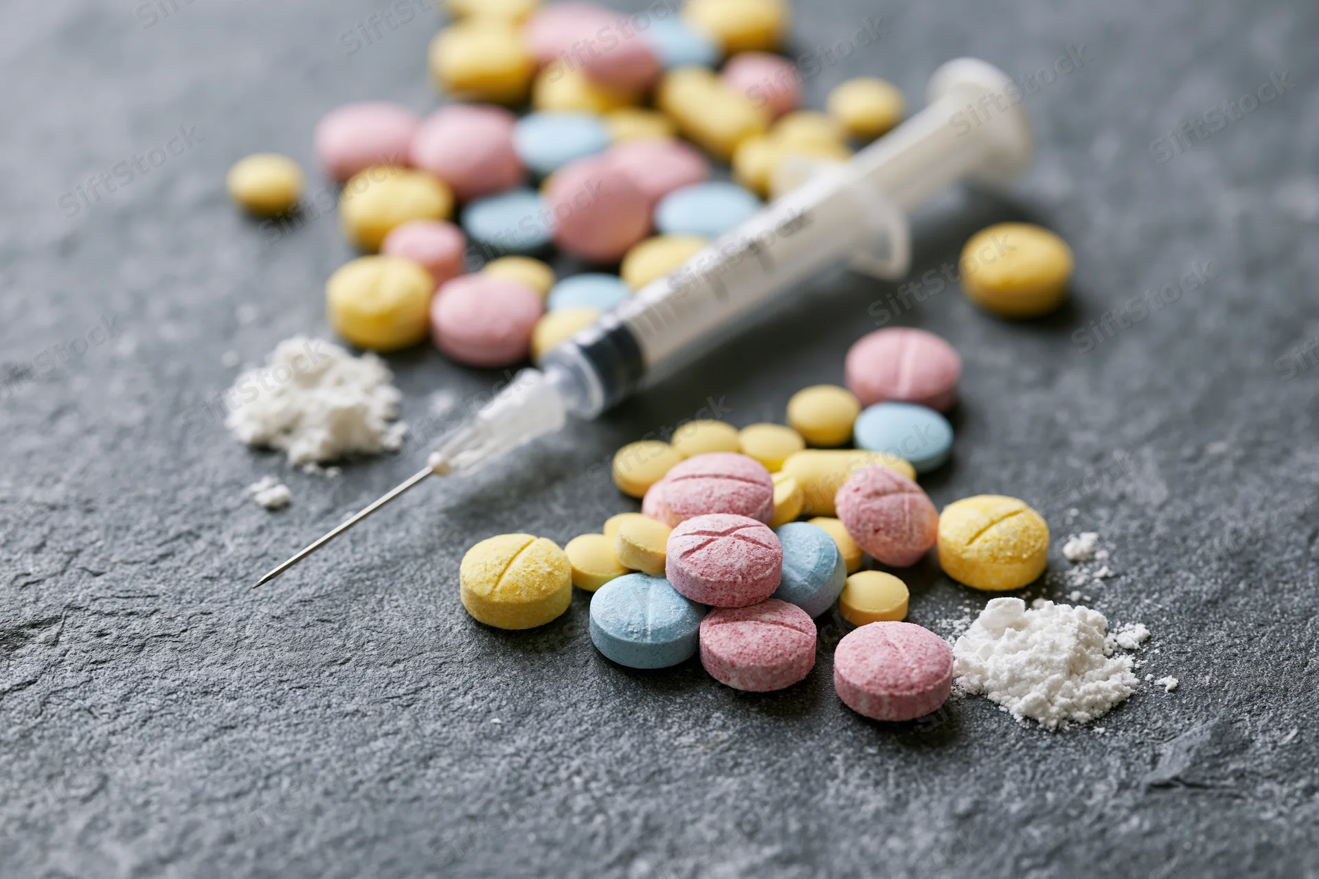 Syringe and colorful pills with powder scattered on a gray stone surface