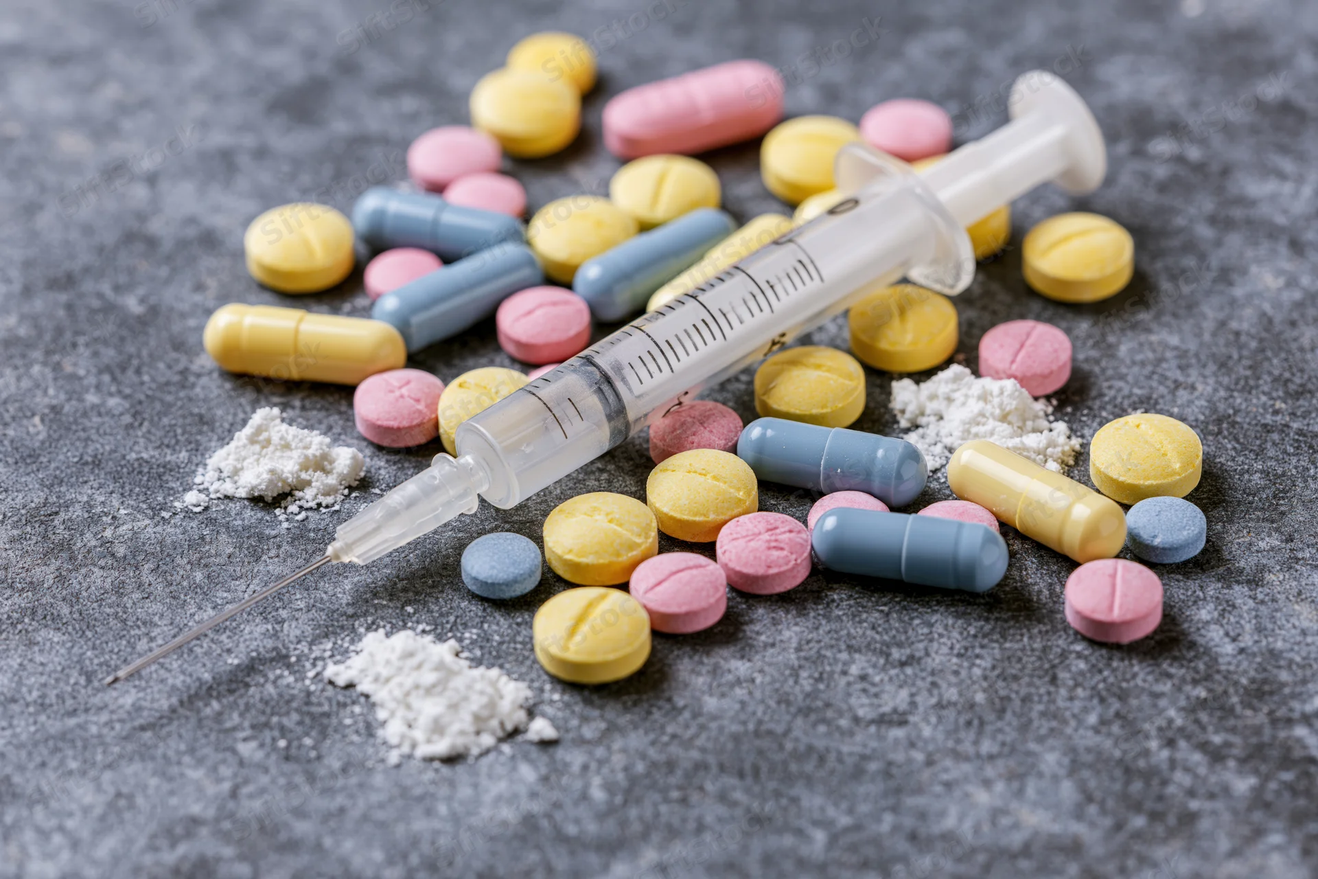 Syringe and assorted pills and powder arranged on a gray surface