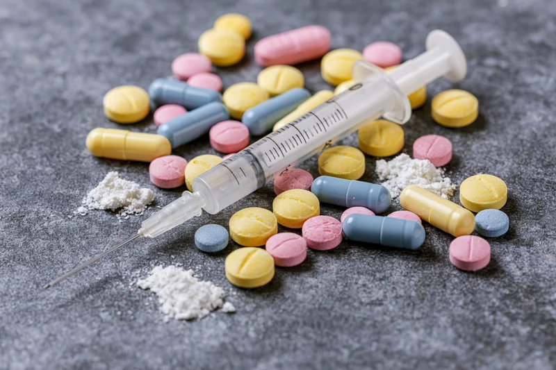 Syringe and assorted pills and powder arranged on a gray surface