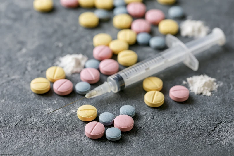 Syringe and scattered colorful pills with powder on a gray textured surface