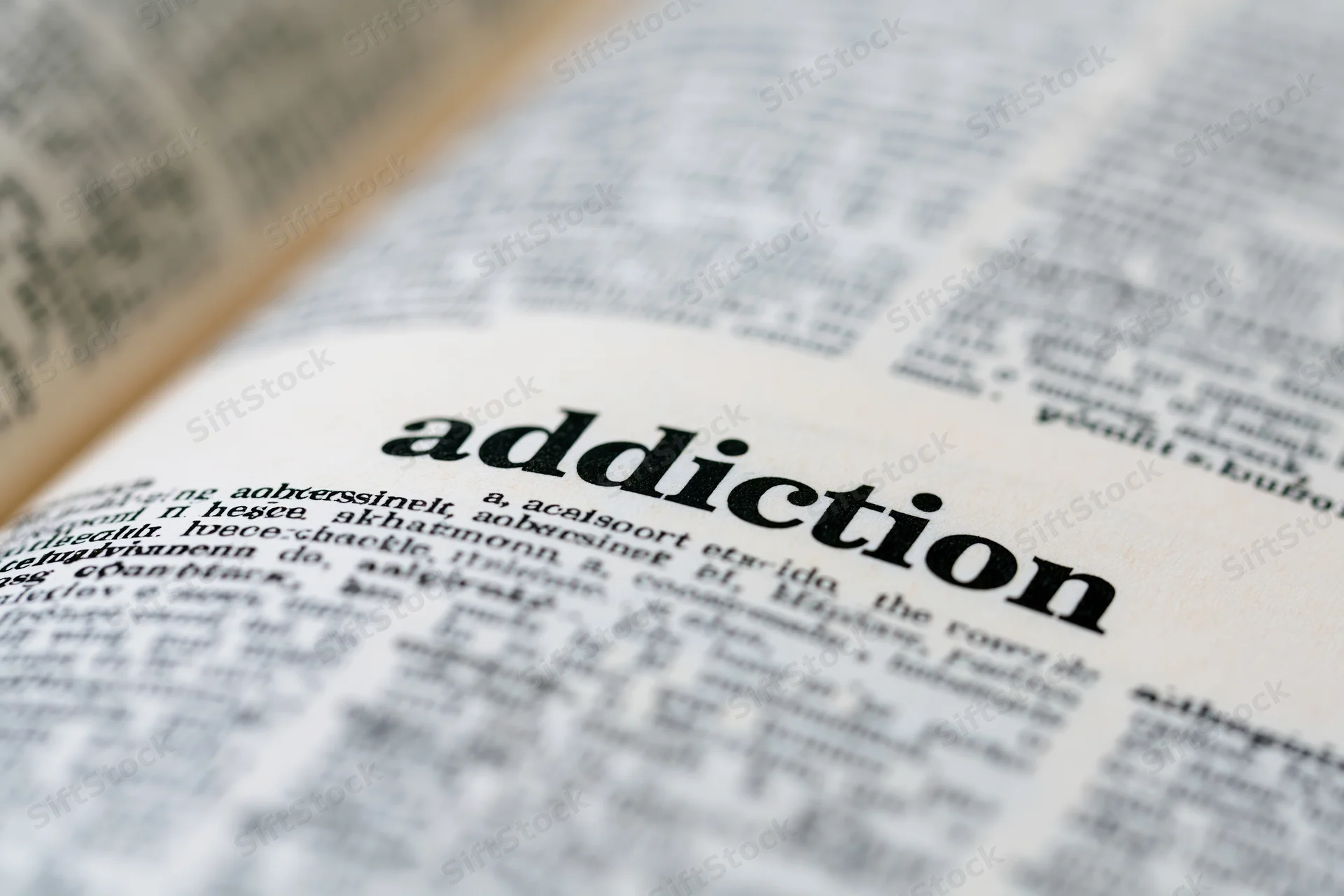 Close-up of open dictionary page showing the word addiction in focus with blurred surrounding text