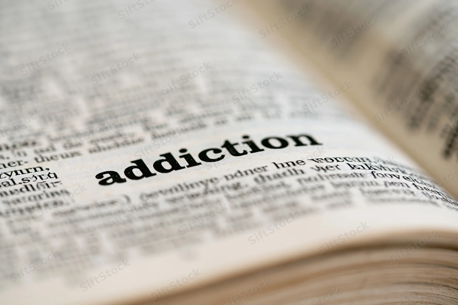 Close-up of open dictionary page showing the word addiction in focus with blurred surrounding text