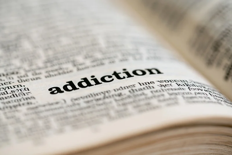 Close-up of open dictionary page showing the word addiction in focus with blurred surrounding text