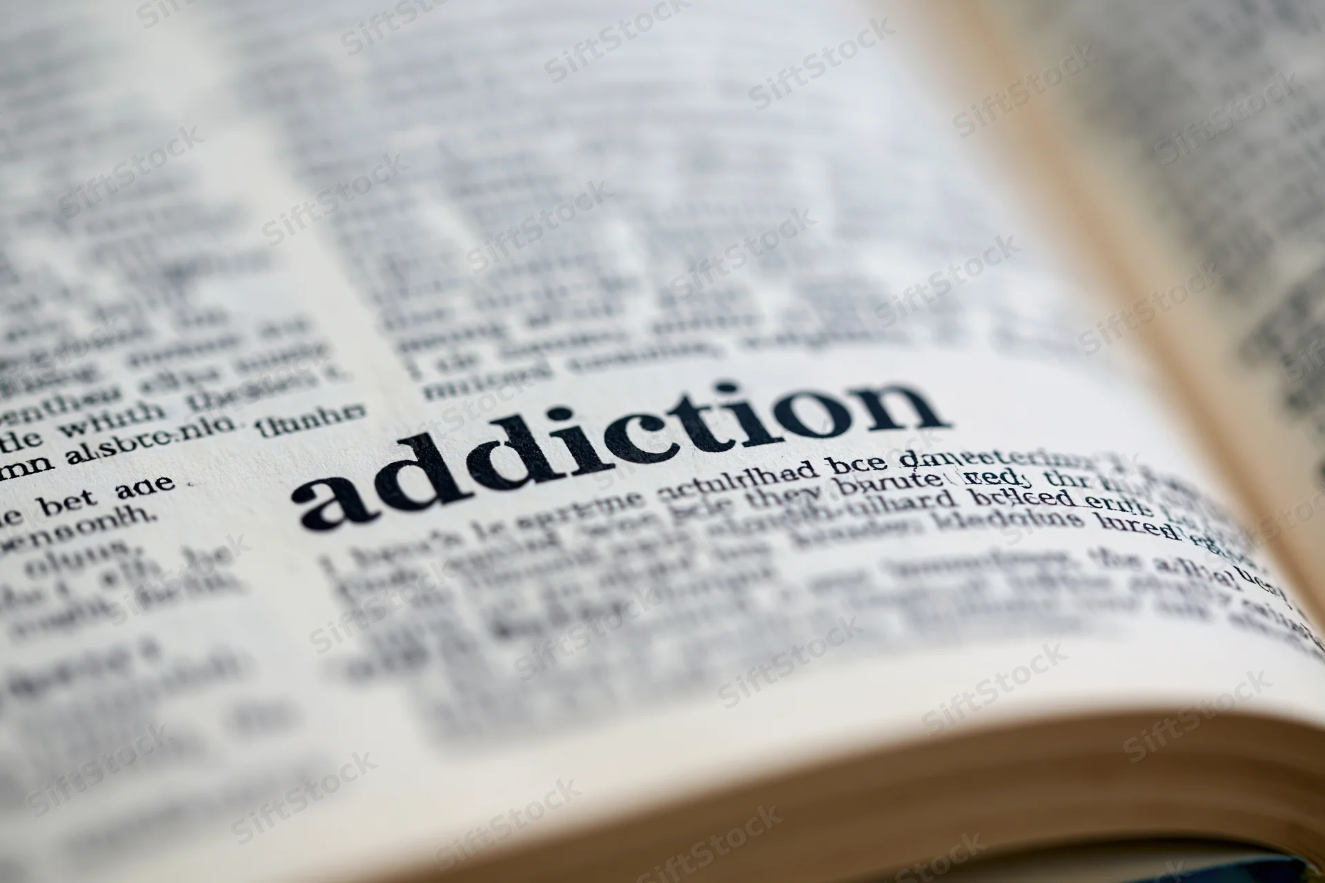 Open dictionary page showing the word addiction in focus with blurred surrounding text