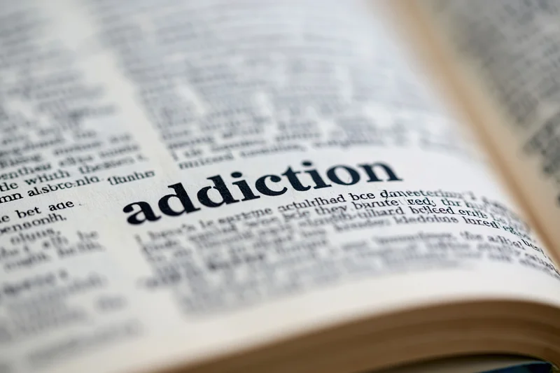 Open dictionary page showing the word addiction in focus with blurred surrounding text