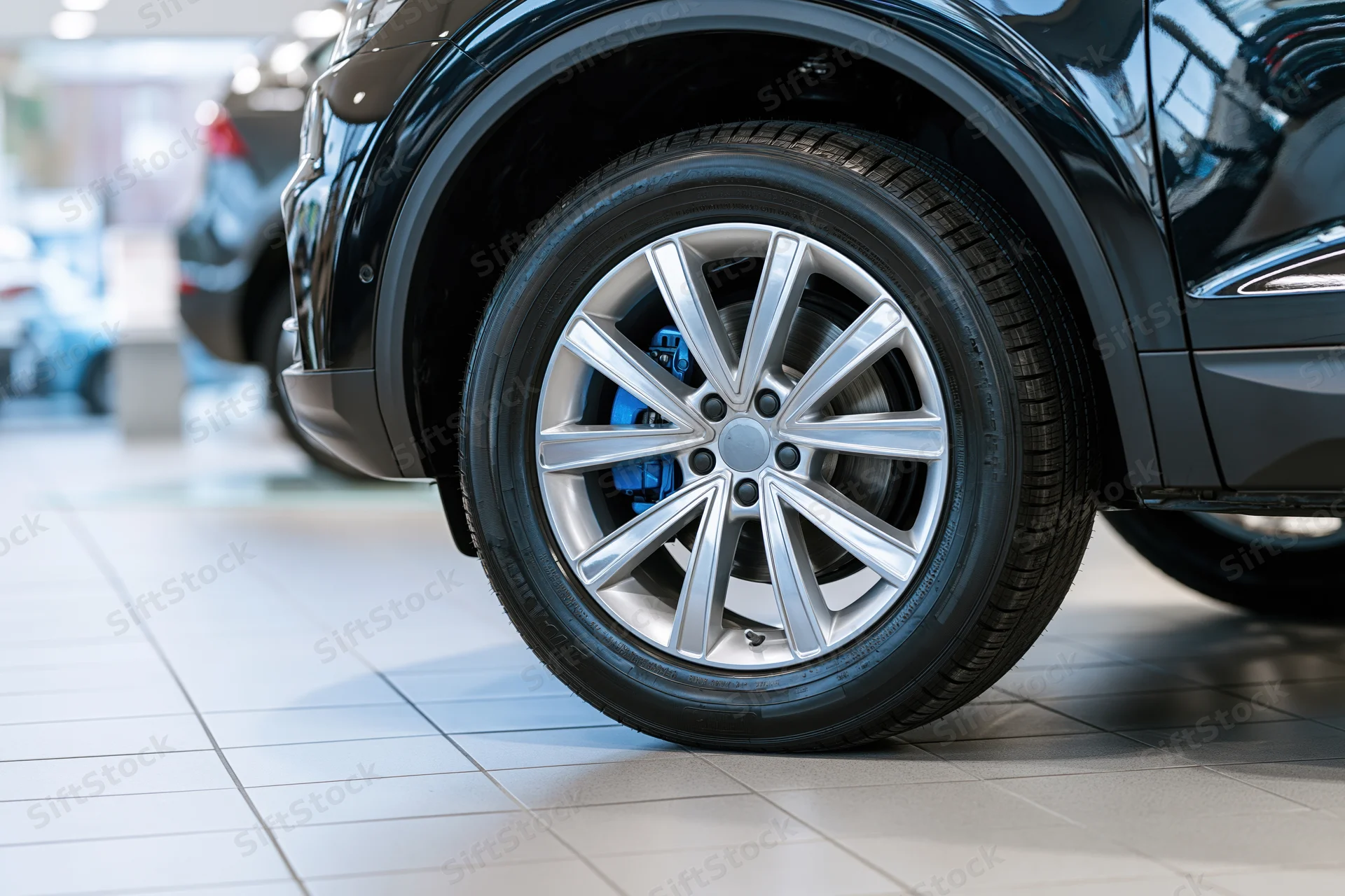 Close-up of a silver alloy wheel on a black car in a showroom