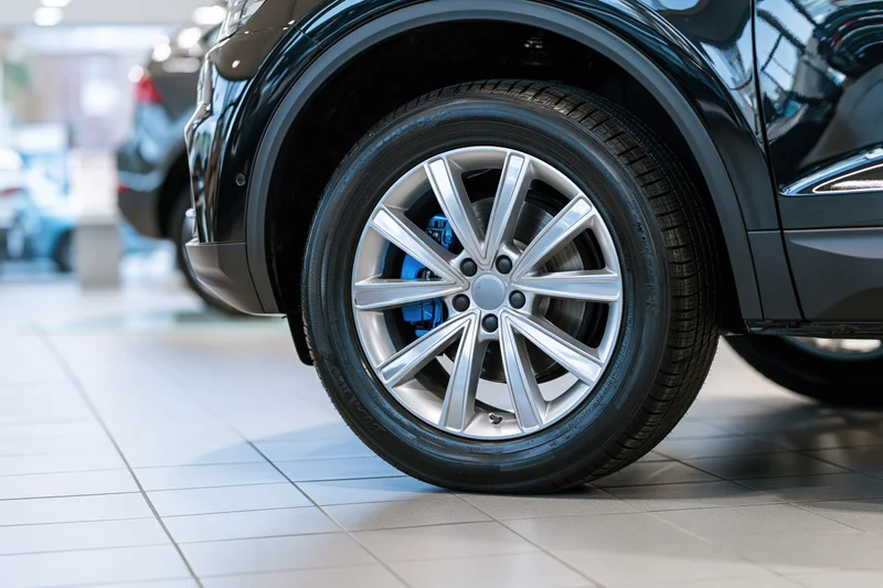 Close-up of a silver alloy wheel on a black car in a showroom