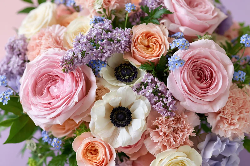 Close-up of a lush mixed flower bouquet with pink roses, peonies, anemones, and lilac against a soft pastel background