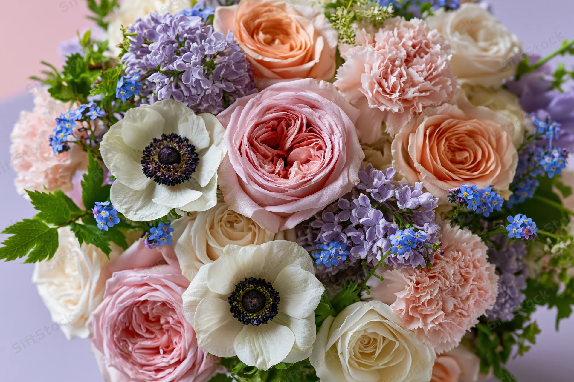Close-up of a lush mixed flower bouquet with pink roses, peonies, anemones and greenery arranged in soft pastel tones