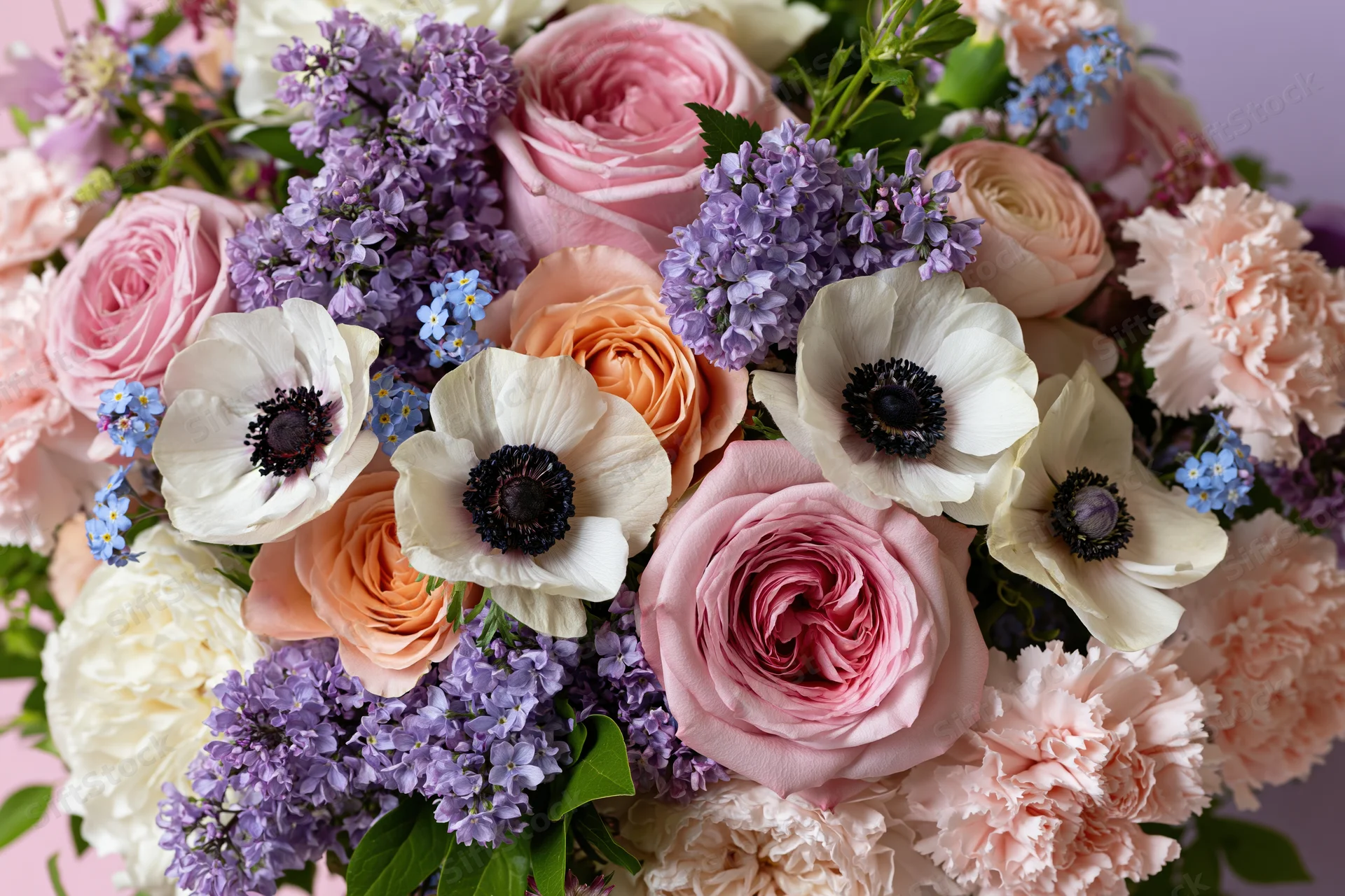 Close-up of a lush mixed flower bouquet with pink roses, purple lilac, white anemones and greenery arranged in soft pastel tones