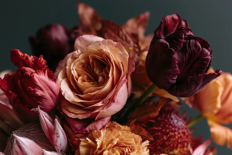 Close-up of a richly layered autumn floral arrangement featuring roses, tulips and carnations in deep burgundy, peach and orange tones