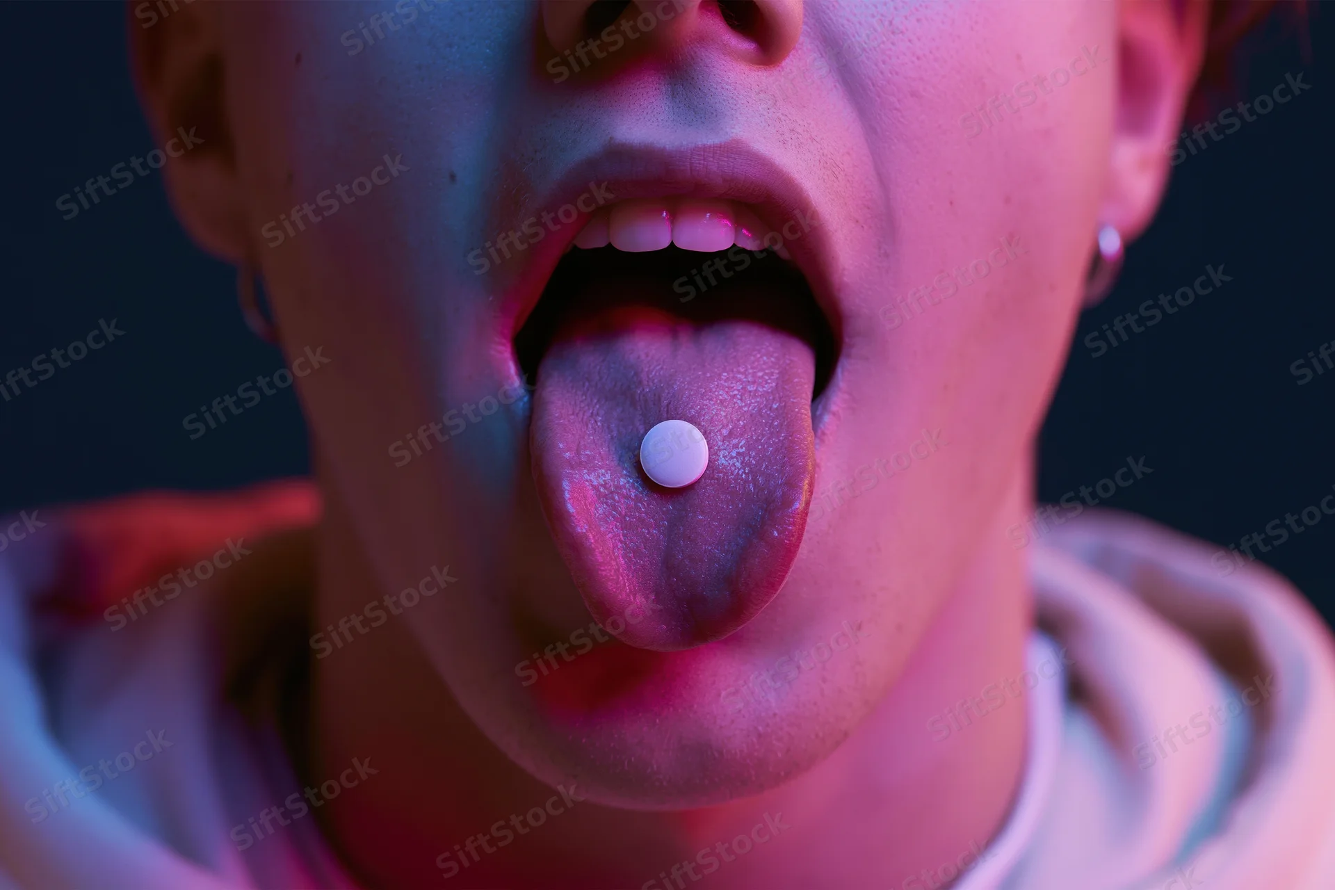 Young person extending tongue with pill under neon pink and blue light