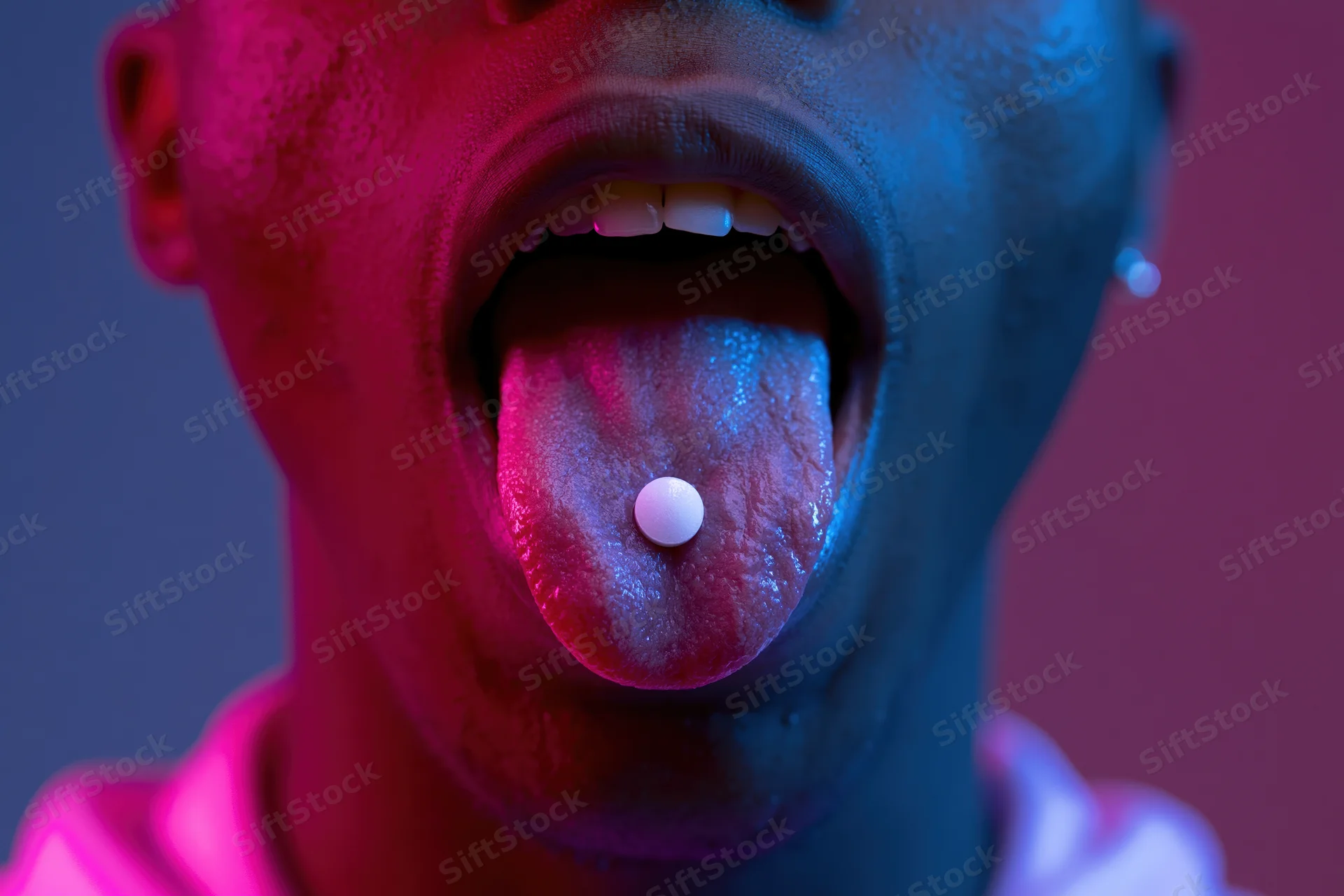 Young african man with tongue extended holding white pill under neon pink and blue lighting