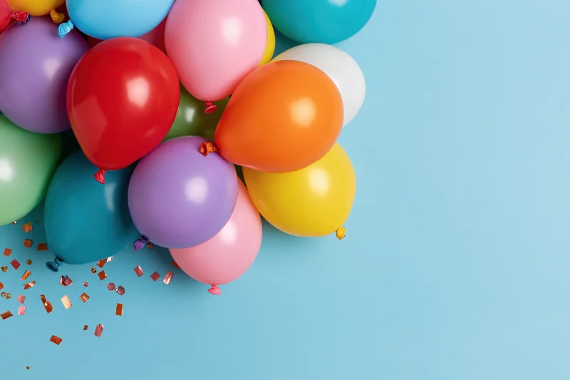 Cluster of multicolored latex balloons with confetti on light blue background