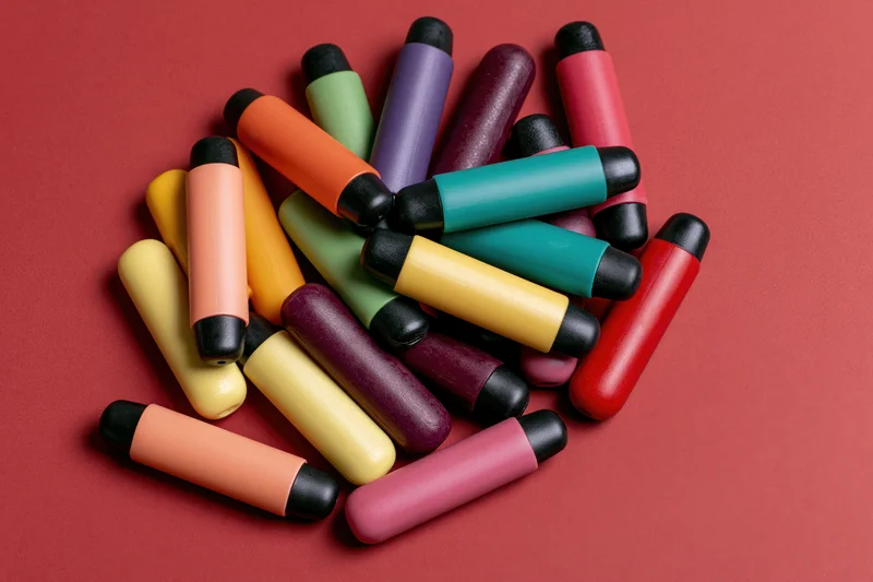 Colorful disposable vape pens scattered loosely on red background