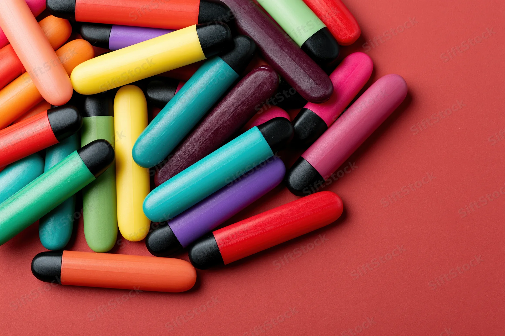 Colorful disposable vape pens scattered on red background with copyspace