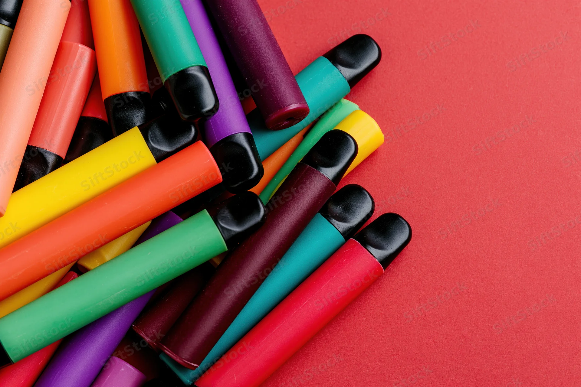 Colorful disposable vape pens scattered loosely on red background with copyspace