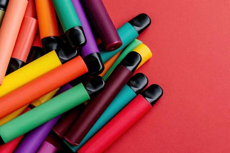 Colorful disposable vape pens scattered loosely on red background with copyspace
