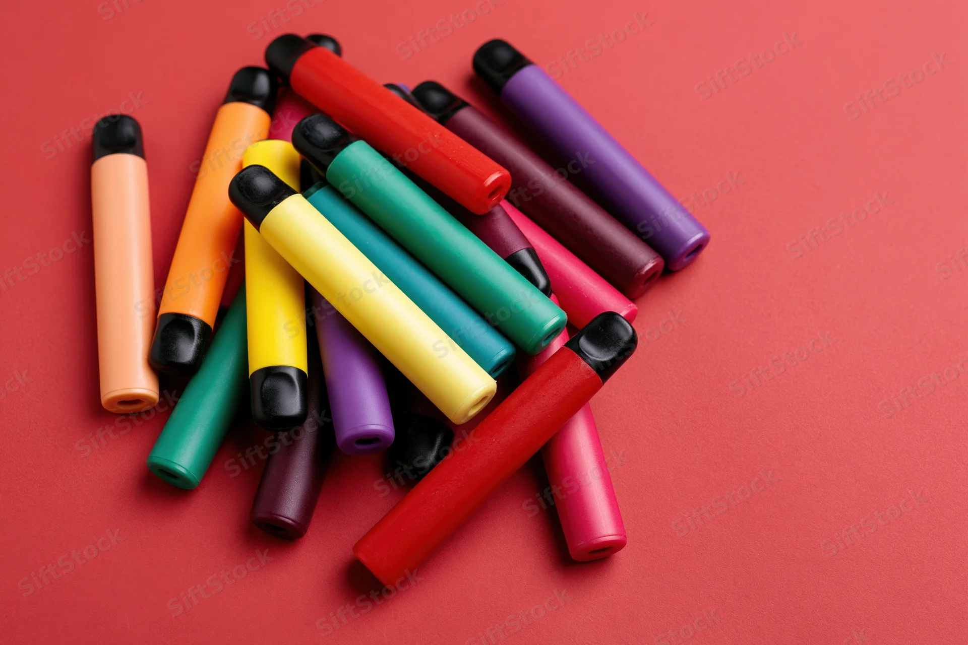 Colorful disposable vape pens scattered loosely on red background