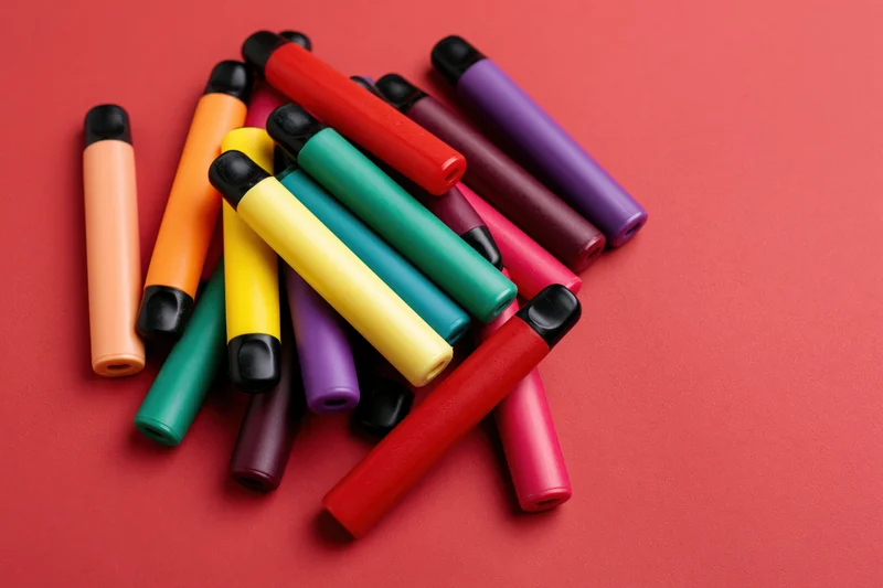 Colorful disposable vape pens scattered loosely on red background