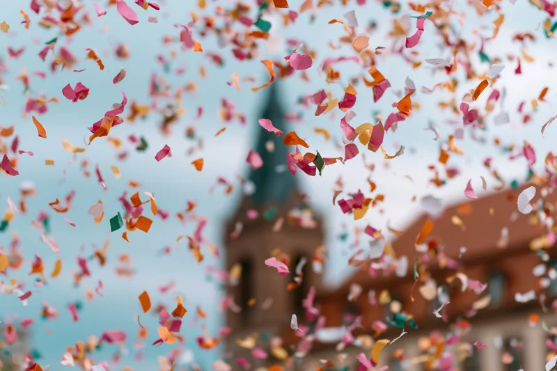 Colorful confetti pieces flying midair in front of a church steeple against a blue sky