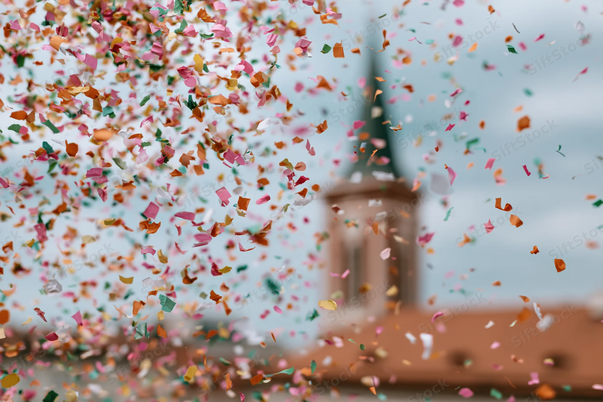 Colorful confetti pieces floating midair in front of a blurred building with a tower and terracotta roof