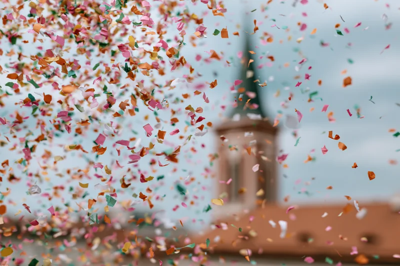 Colorful confetti pieces floating midair in front of a blurred building with a tower and terracotta roof