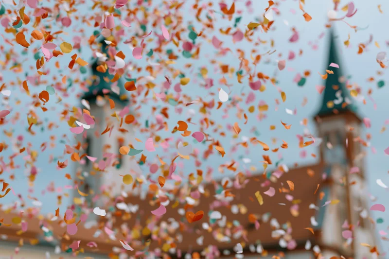 Colorful confetti pieces floating midair in front of a church steeple against a blue sky