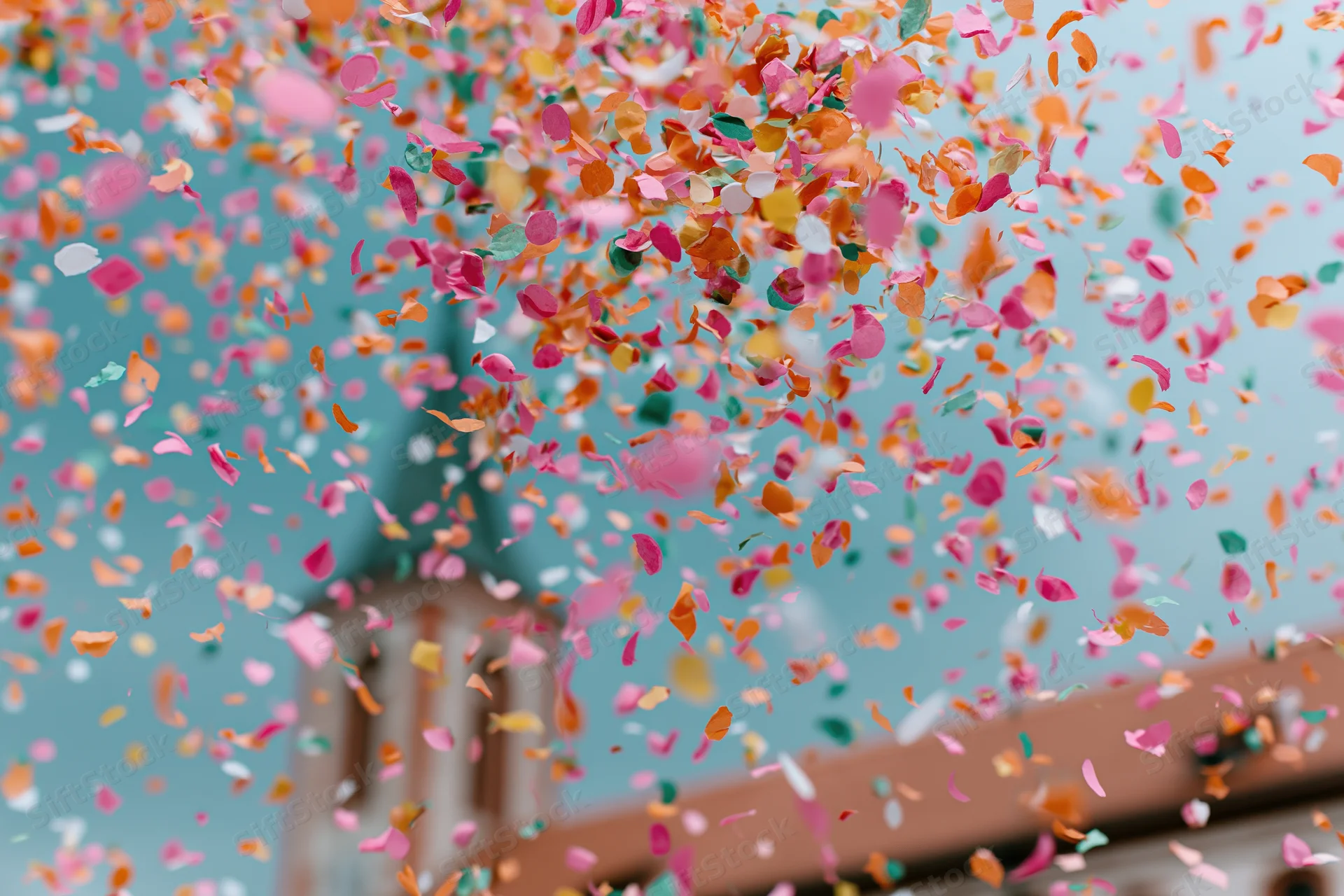 Colorful confetti bursting in mid-air against a blue sky with a church steeple in the background