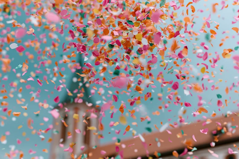 Colorful confetti bursting in mid-air against a blue sky with a church steeple in the background