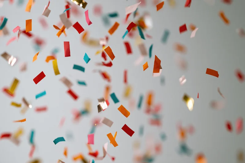 Colorful paper confetti pieces falling midair against a light background