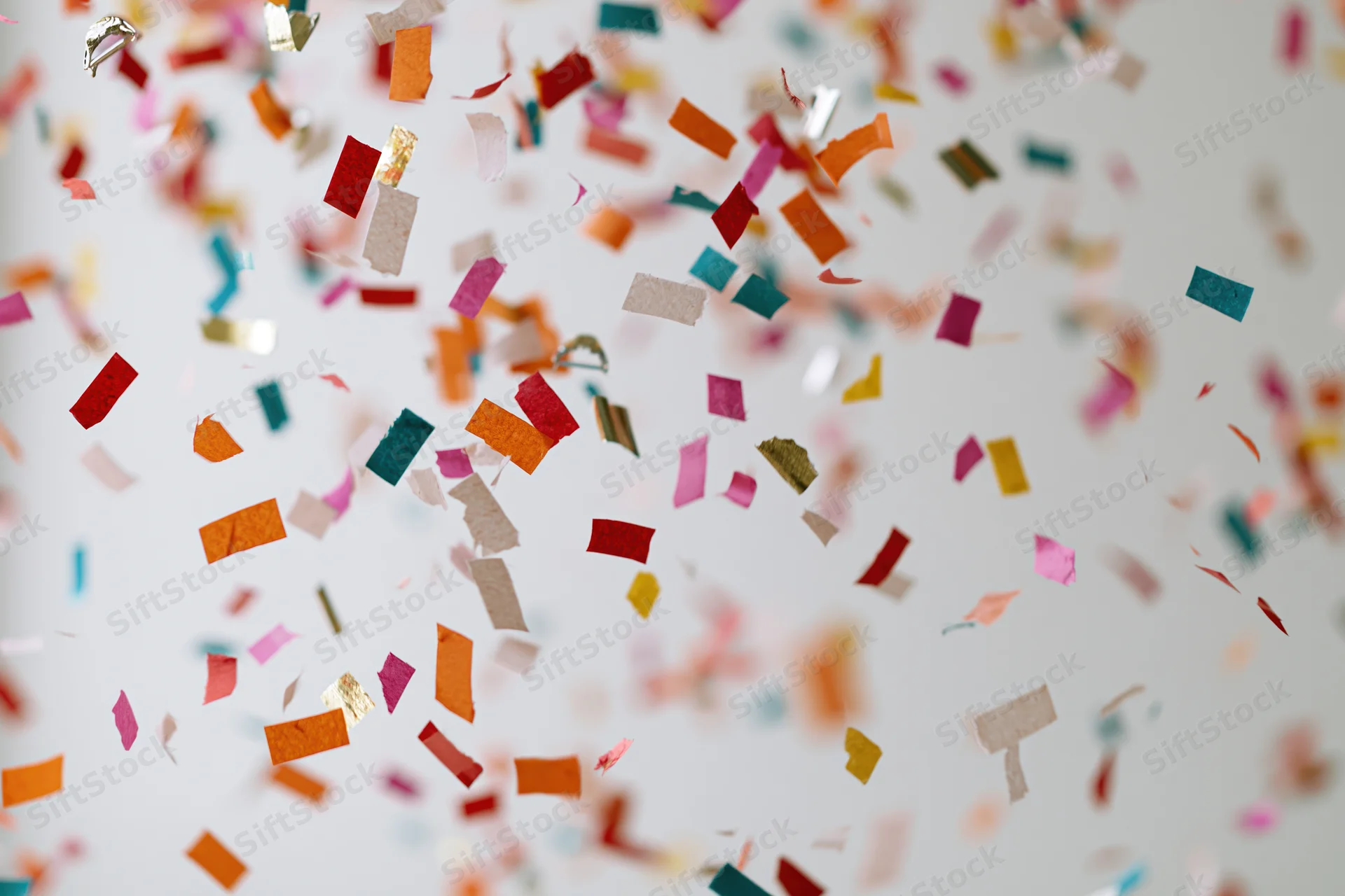 Colorful paper confetti pieces falling midair against a white background