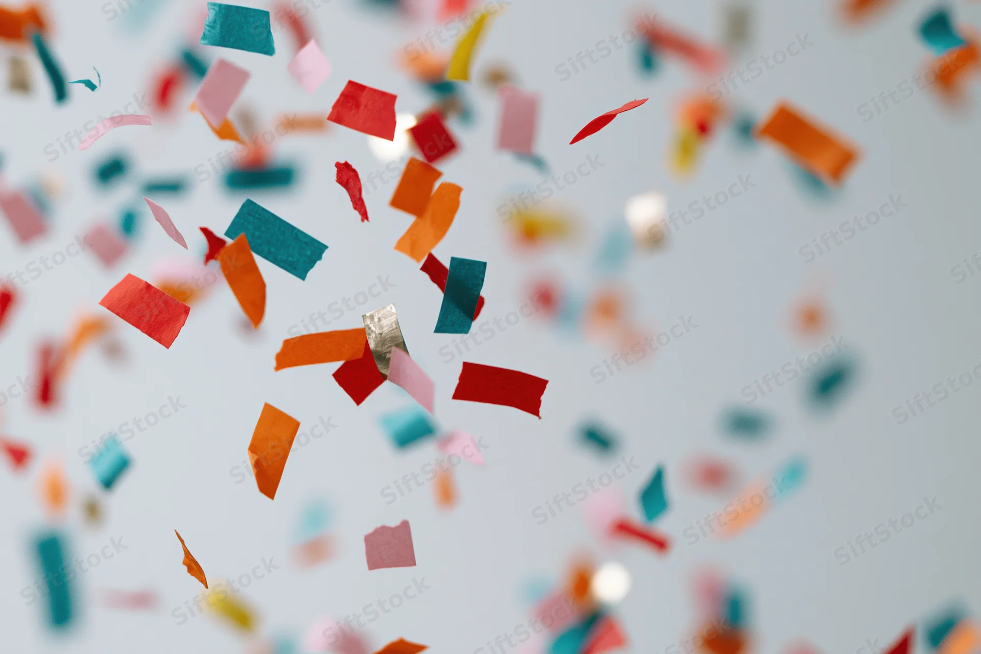 Colorful paper confetti pieces falling midair against a light background with scattered copyspace