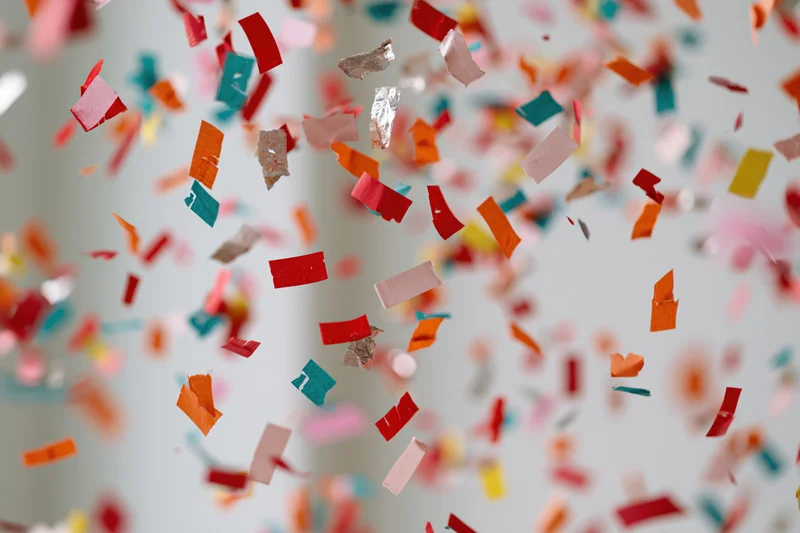 Colorful paper confetti pieces falling midair against a light background with copyspace
