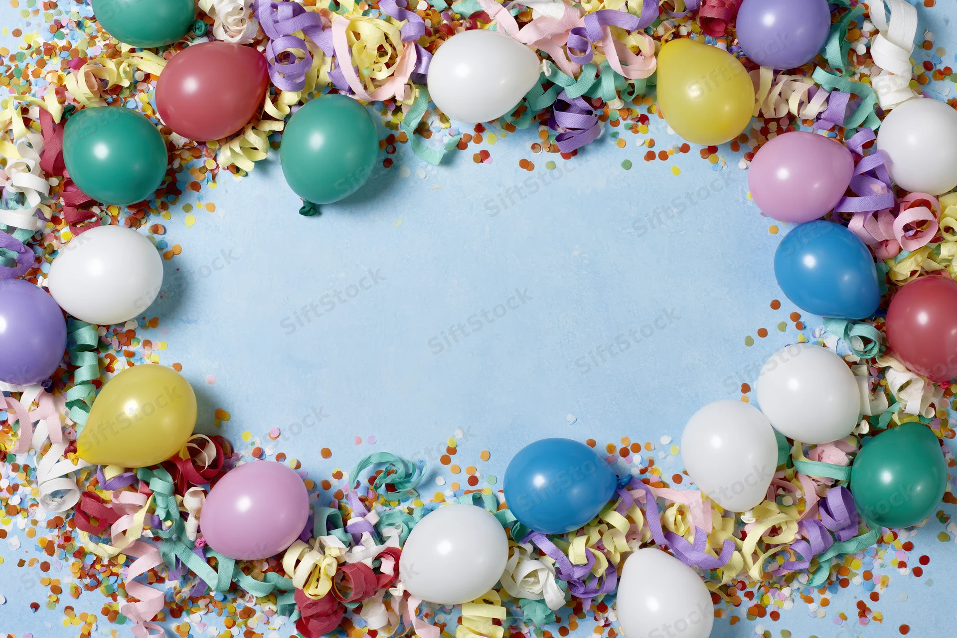 Colorful party balloons and curled paper streamers arranged in a circular frame on a blue surface with confetti and copyspace