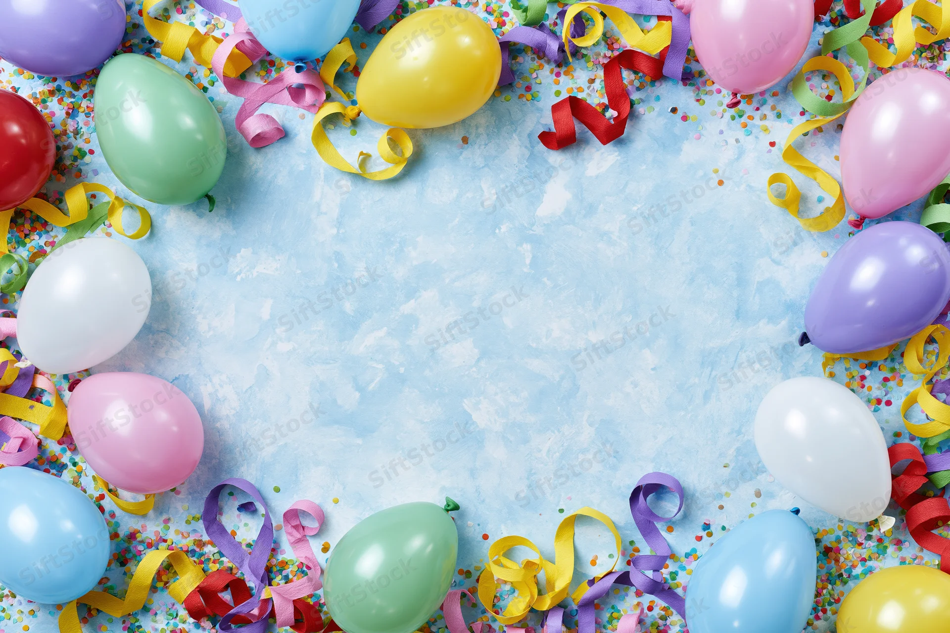 Colorful party balloons and curled paper streamers arranged in a border around a blue textured surface with confetti, leaving central copyspace