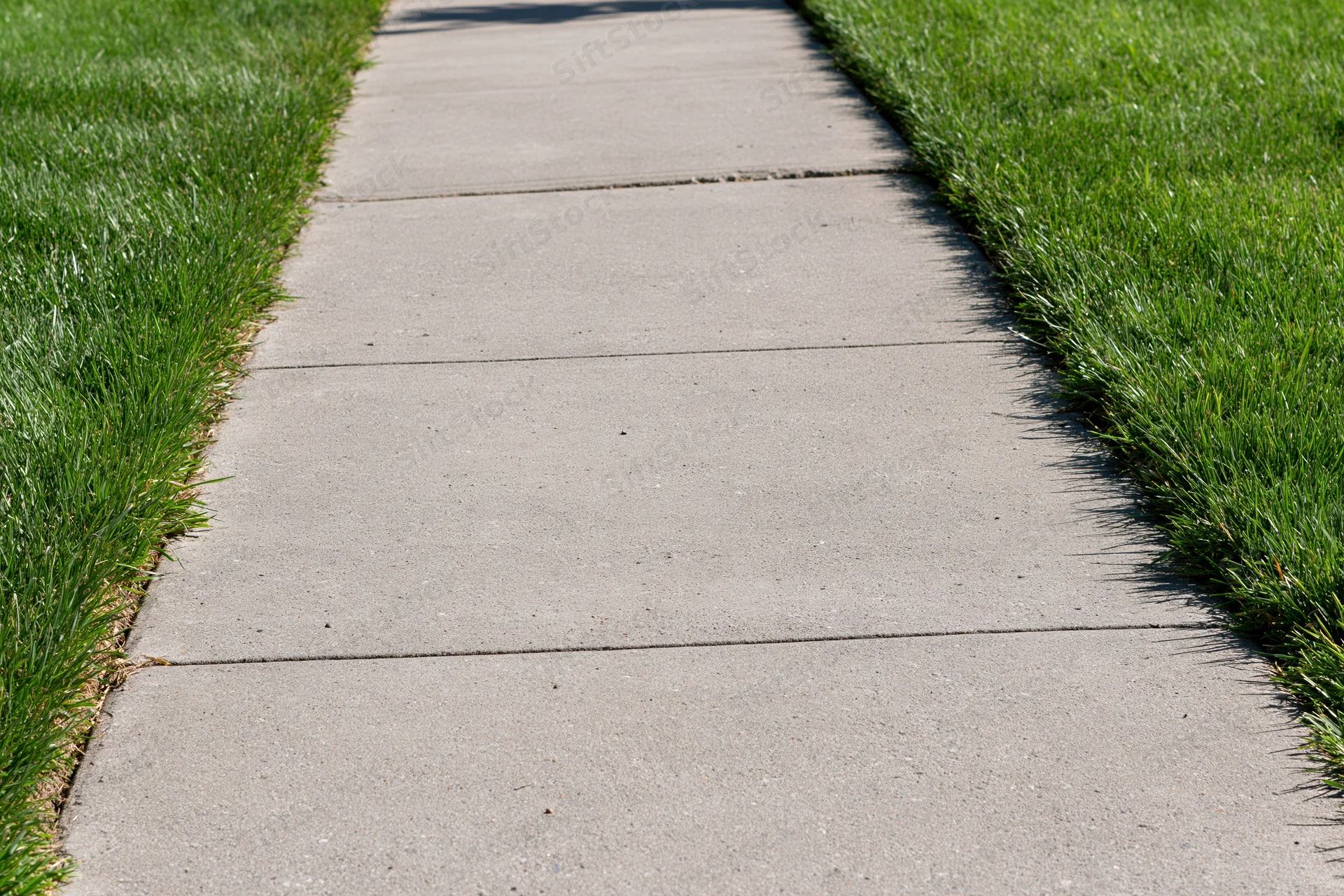 Concrete sidewalk bordered by green grass leading into the distance
