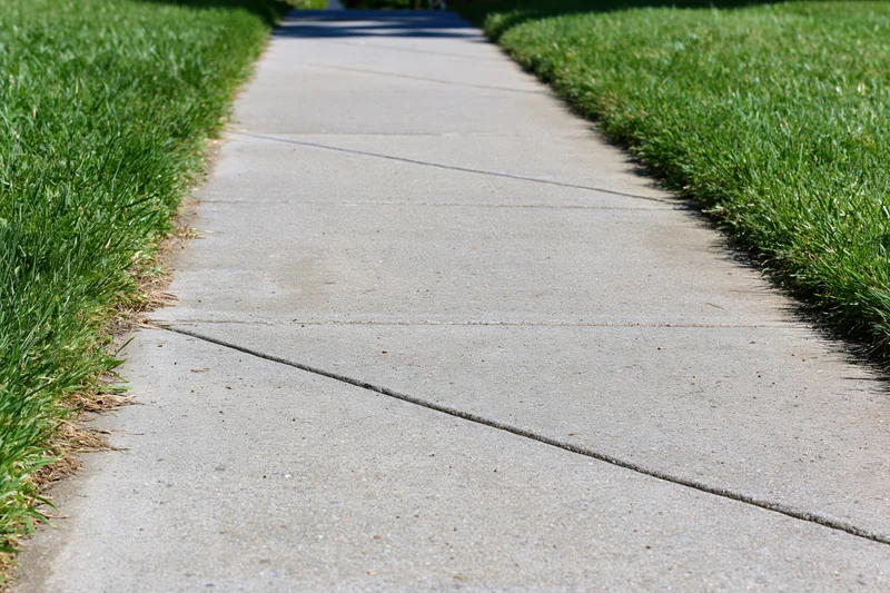 Concrete sidewalk with expansion joints running diagonally between green lawns in a residential area