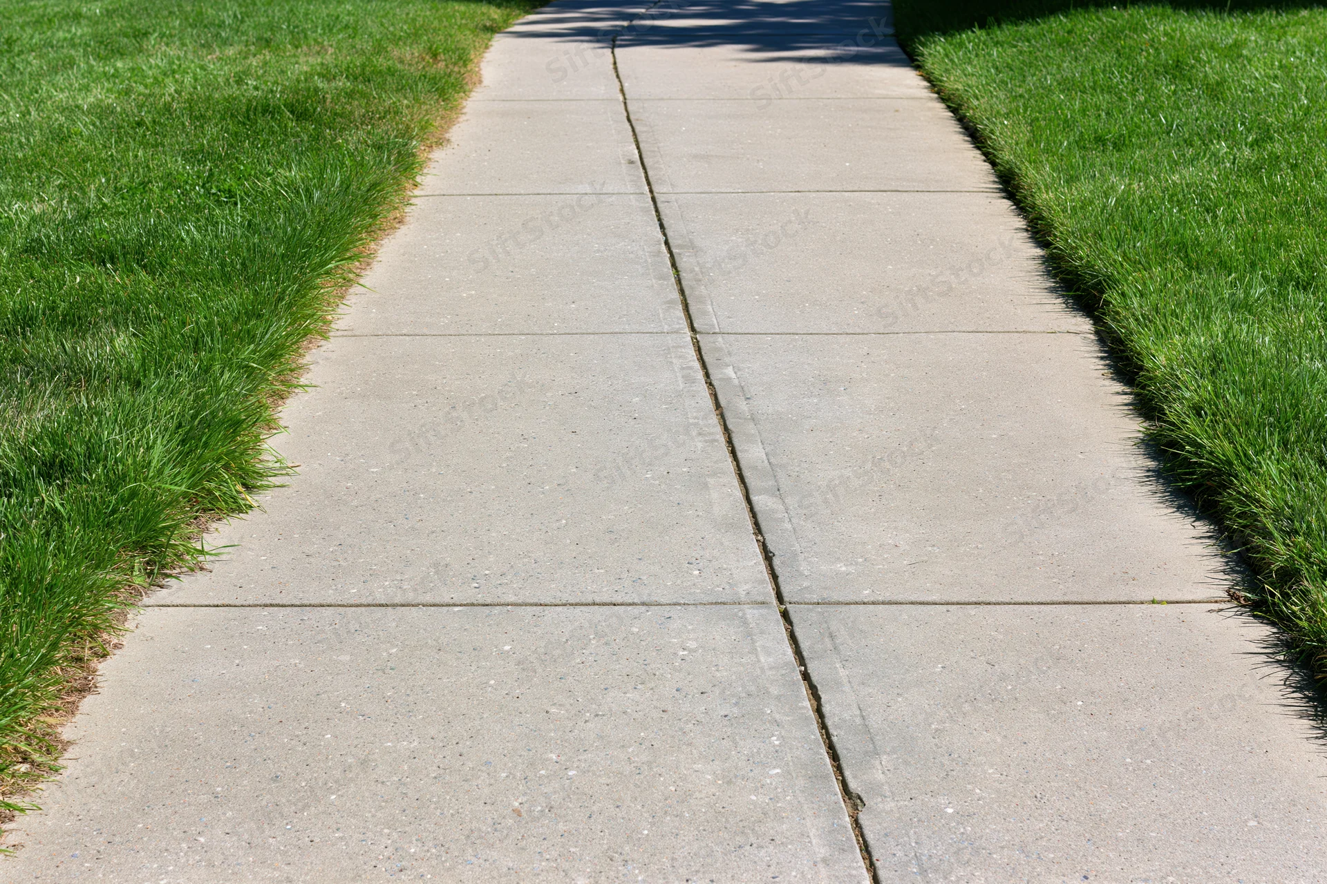 Concrete sidewalk with expansion joints running diagonally between green lawns in a suburban yard