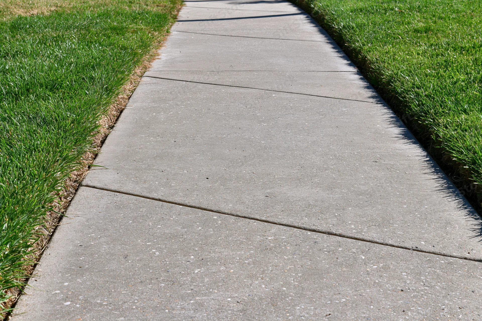 Concrete sidewalk with expansion joints running diagonally between green grass lawns