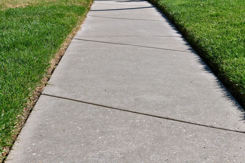 Concrete sidewalk with expansion joints running diagonally between green grass lawns