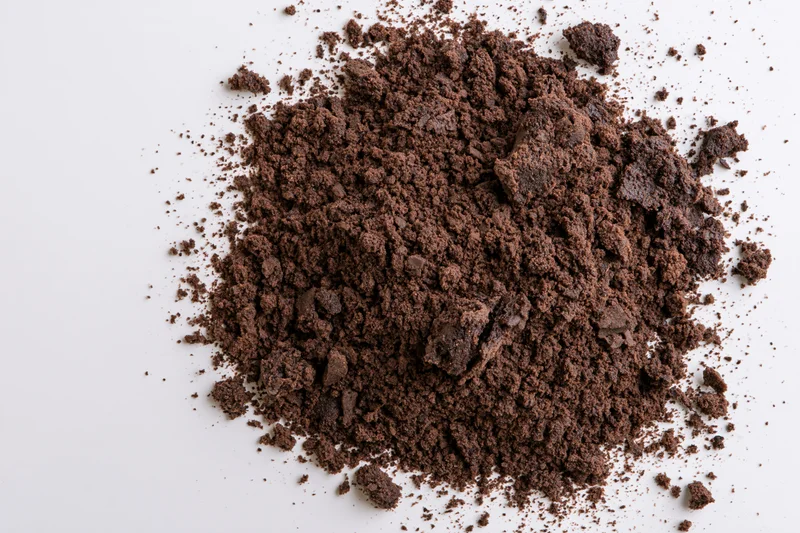 Pile of dark brown chocolate cake crumbs scattered on white surface