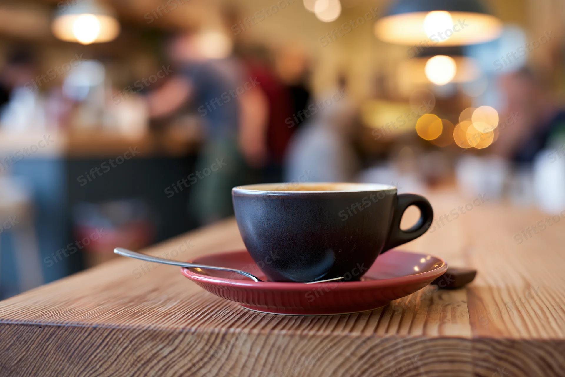 Dark ceramic espresso cup with spoon on red saucer on wooden table in cafe interior
