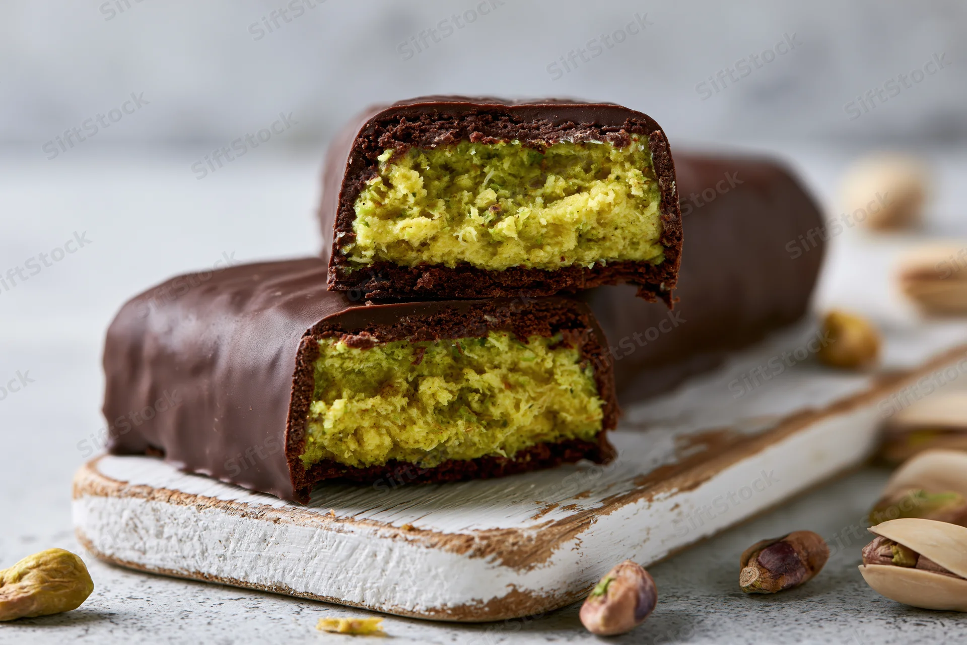 Chocolate bar broken in half revealing green pistachio filling on a white wooden board