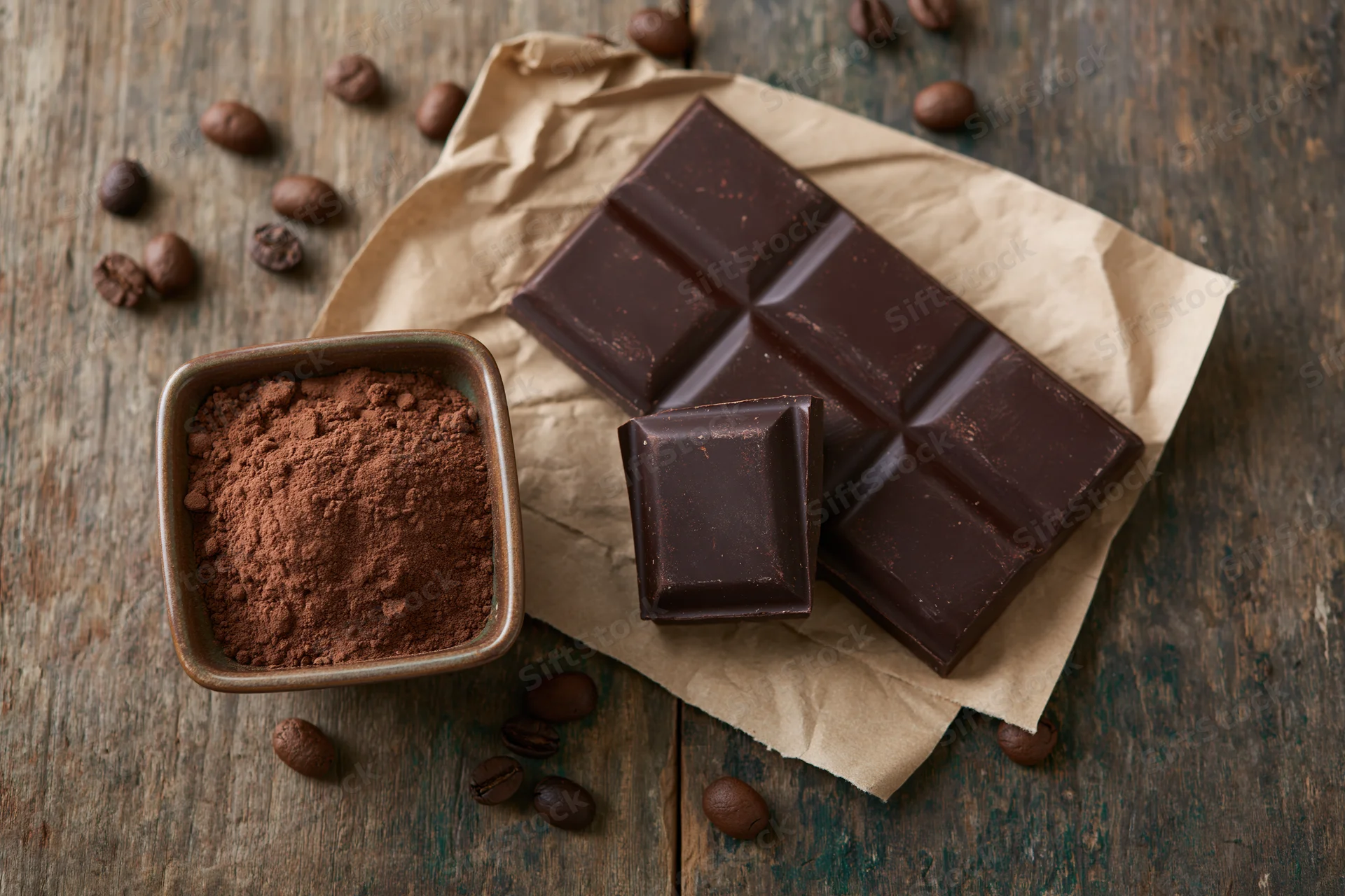 Dark chocolate bar with broken square and cocoa powder on crumpled paper over wooden table