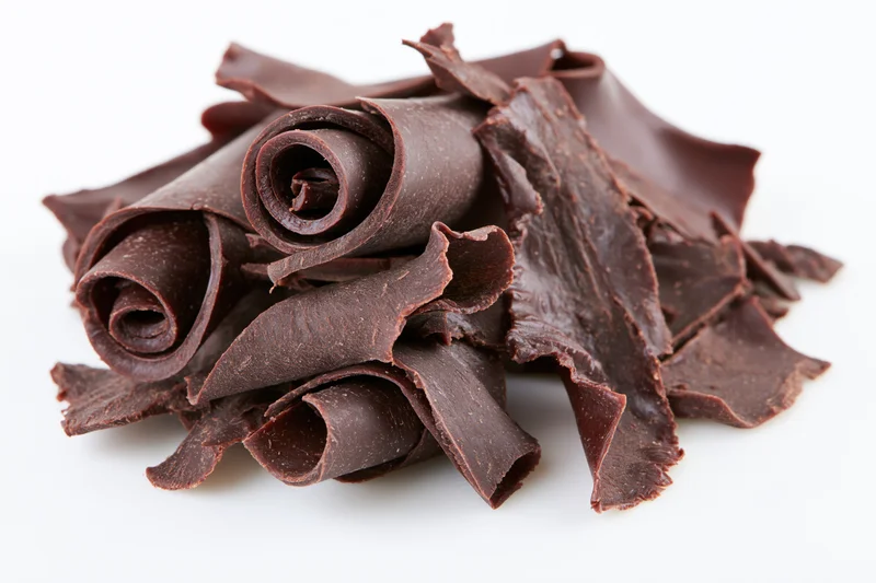 Dark chocolate curls and shavings piled together on white background