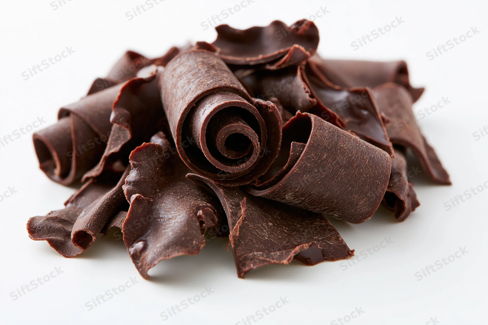 Dark chocolate curls and shavings piled loosely on white background