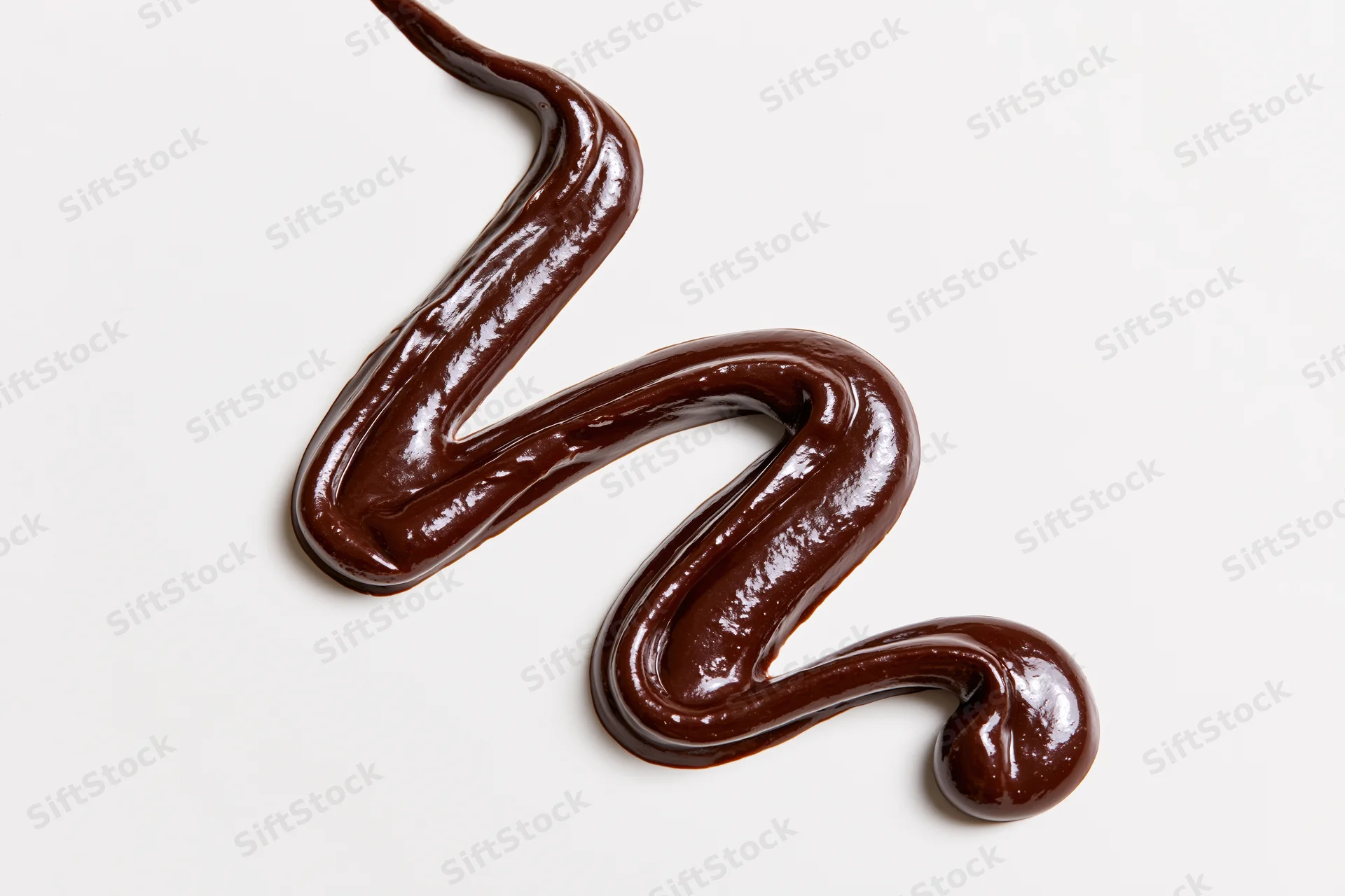 Dark chocolate sauce drizzled in a loose zigzag swirl on white background