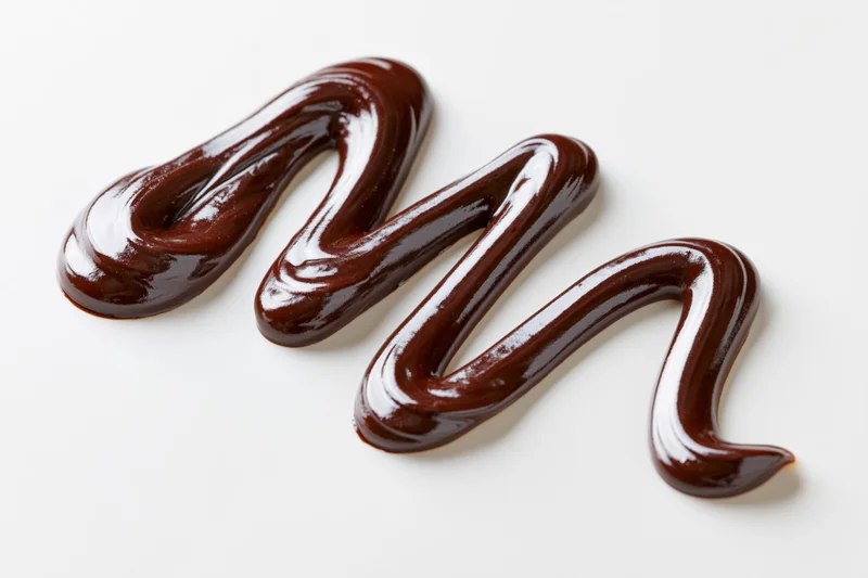Dark chocolate sauce drizzled in a loose zigzag swirl on white background