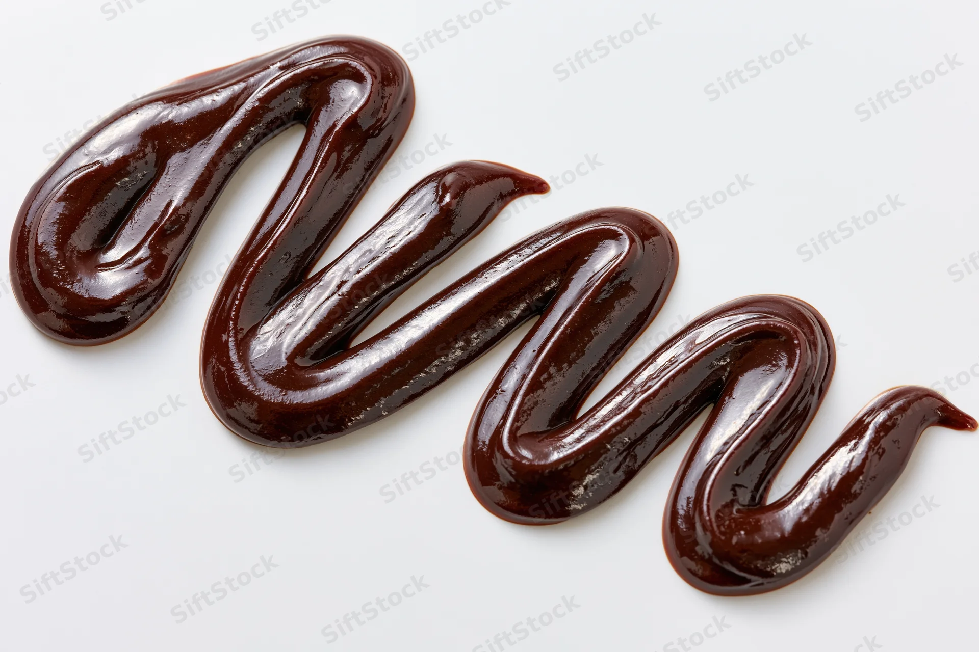 Dark chocolate sauce drizzled in a loose zigzag swirl on white background